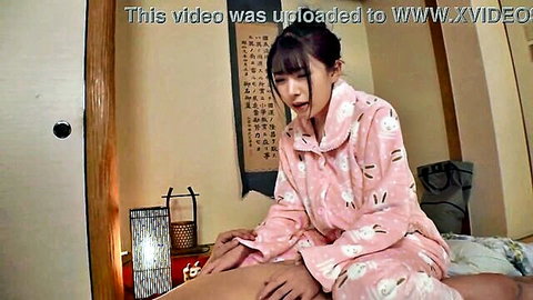 Japanese woman in pink pajamas sitting on bed, touching her leg seductively