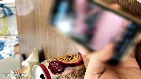 Hand gripping red Wangzai milk drink can on wooden surface with snacks