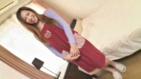 Cute smiling Japanese brunette in red polka dot apron over blue top posing in bedroom