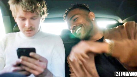 Blonde white guy and smiling black stud checking phone together in car backseat