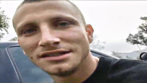 Close-up of shaved-head white guy with stubble smirking from car window outdoors