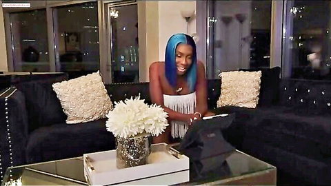 Busty blue-haired woman in skimpy fringed top smiling teasingly on luxury couch