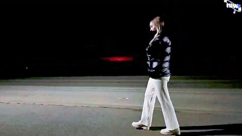 Alina Rai in black puffer jacket and white pants, walking at night outdoors