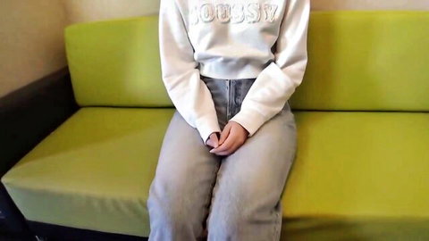 Young woman in white hoodie and gray jeans sits casually on couch