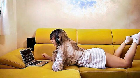 Blonde stepsis in short dress lounging on couch with laptop and headphones