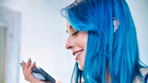 Jewelz Blu with vibrant blue hair smiles seductively while holding a phone, teasing lesbian preview