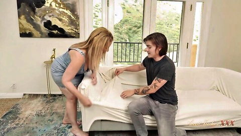Blonde MILF in short dress assists tattooed guy with couch cover in steamy setup