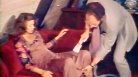 Vintage suited man kisses and stimulates hairy pussy with wand on busty woman's exposed tits on red couch