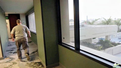 Man walking down hotel hallway with pool view through large windows