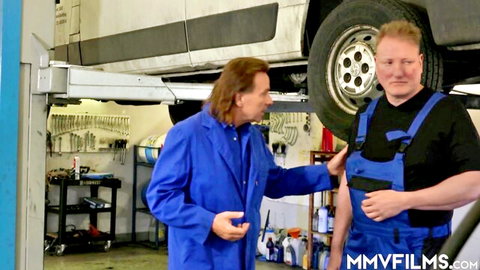 Two mechanics in blue uniforms chatting beside lifted white van in garage workshop