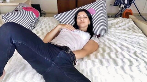 Busty brunette in tight jeans spreads legs teasingly on bed