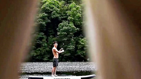 Cody Seiya shirtless outdoors by river on paddleboard, muscular build