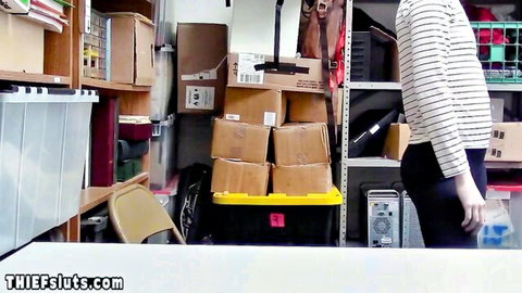 Katy Kiss in striped shirt posing in cluttered storage room