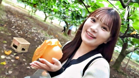Cute young Asian girl smiling while holding large orange in orchard