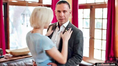 Blonde babe in blue dress embraces suited man from behind touching his chest intimately