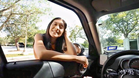 Busty Asian babe smiling with deep cleavage leaning out car window in parking lot