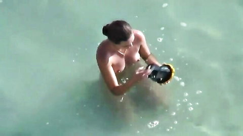 Brunette babe topless in shallow beach water, holding object