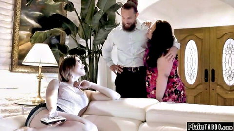 Skinny brunette teen in tank top smiles up at bearded stud while curvy dark-haired babe hugs him on couch