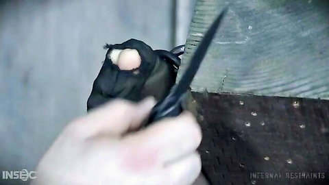 Dominant hand slicing through tight black bondage restraints with sharp knife in intense BDSM scene