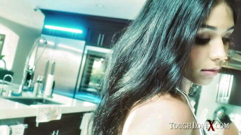 Seductive young brunette with long dark hair and choker necklace posing in modern kitchen