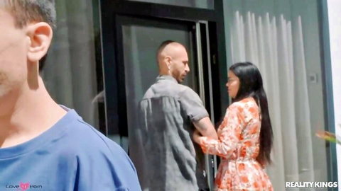 Brunette MILF in floral dress greets muscular man at door while husband watches