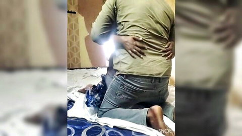 Man in green shirt hugs woman from behind on bed with pants pulled down