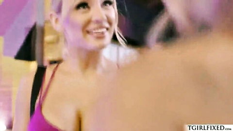 Smiling blonde tgirl babe with big tits in pink top teases guy from behind in living room