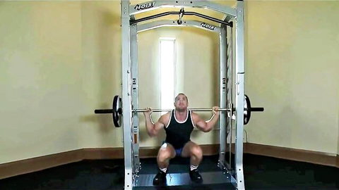 Muscular hunk squatting heavy weights in gym, seducing dominant scene with beautiful ladyboy
