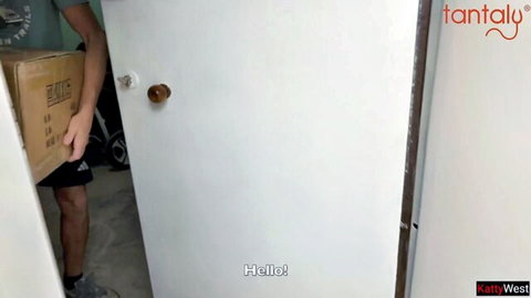Delivery man in Adidas gear holds cardboard box at slightly open white door saying hello
