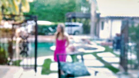 Blonde woman in tight pink dress standing by pool teasing her curves