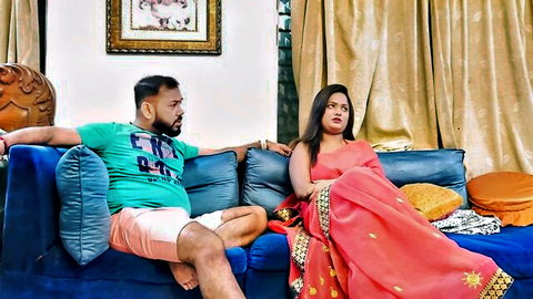 Sexy Indian couple in saree and shorts sitting intimately on blue sofa teasing viewers