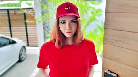 Sexy redhead in red Levi's cap and tight shirt smiling seductively outdoors