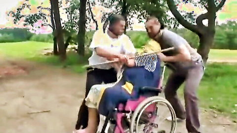 Two black men assisting mature black woman in pink wheelchair outdoors in park