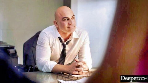 Bald businessman in white shirt and tie sits seriously at office desk