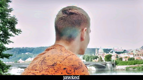 Athletic jock Roque Rems in orange shirt overlooking scenic river bridge