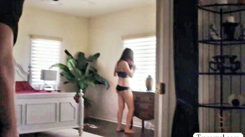 Skinny brunette in black bra and thong panties standing by bedroom window teasing