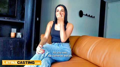 Sexy Latina on casting couch shushing with finger to lips, teasing in tight tank top and jeans