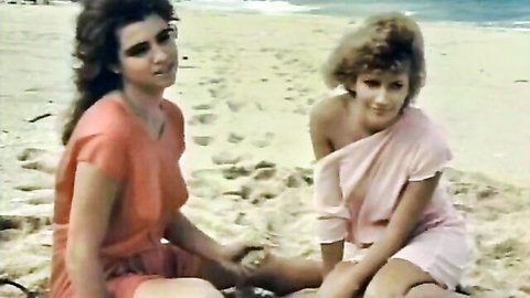 Two sexy babes in orange and pink dresses holding hands on sunny beach