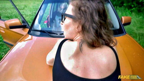 Brunette with glasses bent over orange car hood looking back in tight black top teasing pussy
