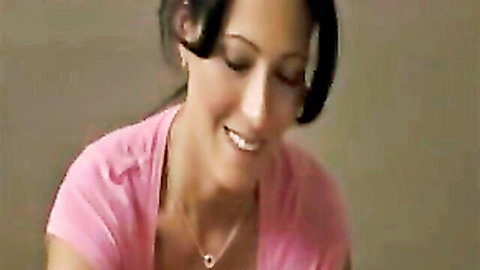 Smiling tanned brunette MILF in pink top showing cleavage and necklace