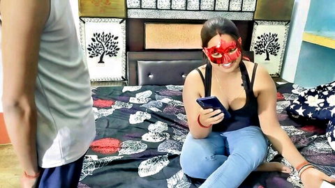 Masked Indian babe in tight tank top flashing deep cleavage sits on bed checking phone while guy watches