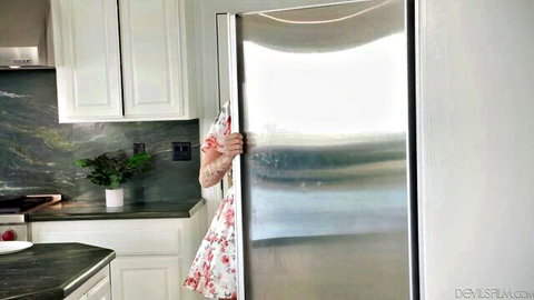 Curvy blonde stepmom peeking teasingly from behind open fridge in short floral dress