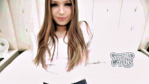 Cute teen babe with long brown hair smiling seductively in tight white top on bed