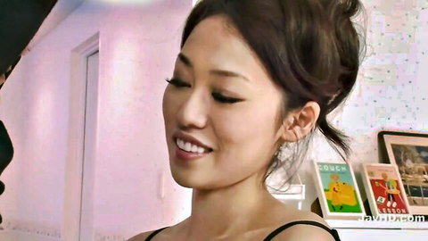 Smiling Asian MILF with dark hair bun in black top, teasing vibe
