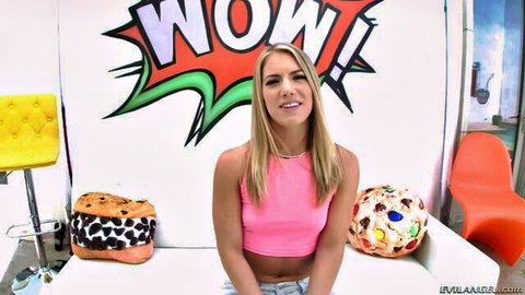 Blonde babe in pink crop top and shorts smiles teasingly against WOW comic wall in studio