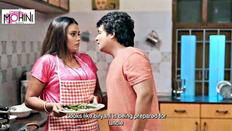 Curvy Indian MILF in pink top and apron holds biryani plate facing young man in kitchen taboo scene