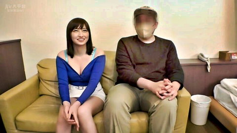 Busty Asian submissive in blue off-shoulder mini dress with blurred man on couch