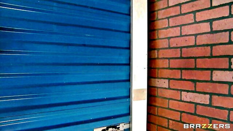 Blue garage door next to red brick wall in Brazzers outdoor porn scene