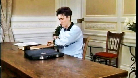 Vintage man in blue shirt sits at wooden desk holding green plant in elegant office room