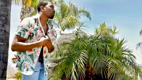 Sexy black stud unbuttons open floral shirt outdoors near palm trees showing toned chest